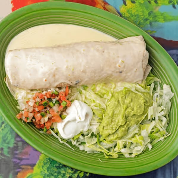 A La Casita burrito covered in white sauce, served with pico de gallo, sour cream, guacamole, and lettuce.