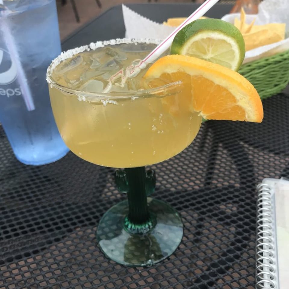 A La Casita margarita with a straw, orange, and lime on a black patio table.