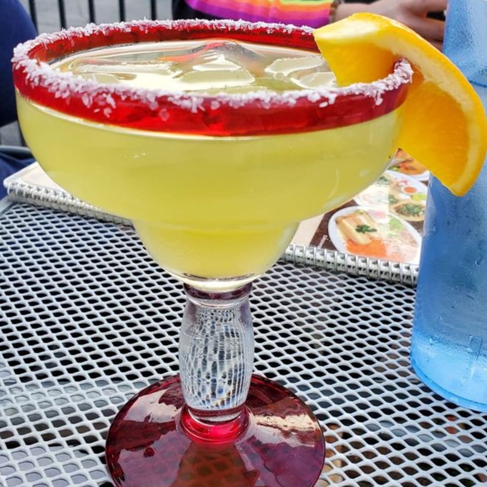 La Casita's bright yellow margarita with a red sugar rim and orange slice on a patio table.